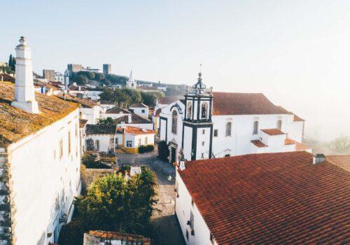 Aerial view medieval Portuguese Obidos over red tiled roofs of buildings in sun shining.